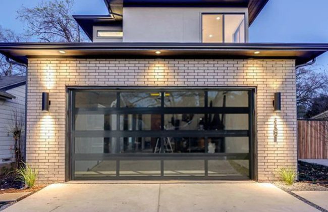 Modern brick house with a glass-panel garage door illuminated by stylish outdoor lighting at dusk.