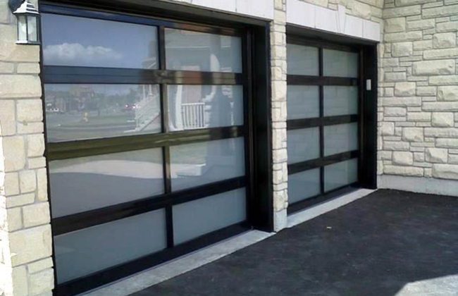 Modern glass garage doors with black frames on a stone residential building.