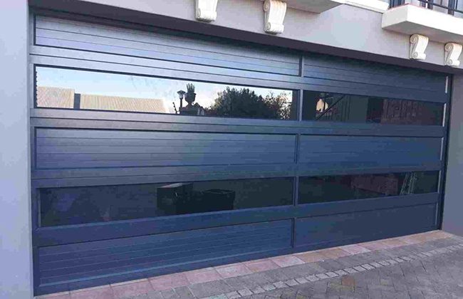 Modern dark-colored glass garage door with horizontal panels, reflecting outdoors, enhances curb appeal of the house.
