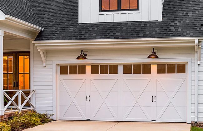 Modern white garage door with crossbuck panels and outdoor lighting. Cozy and stylish exterior design.
