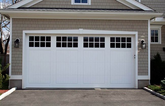 White double garage door with windows on a suburban house, surrounded by exterior lighting and a paved driveway.