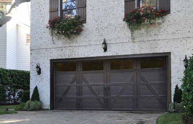 Stylish dark wood garage door on a brick house with flower boxes and outdoor lanterns.