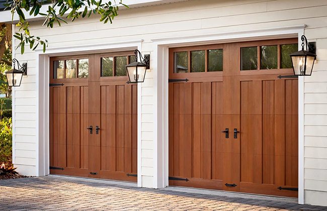 Wooden garage doors with black handles and decorative lanterns on a white building facade.