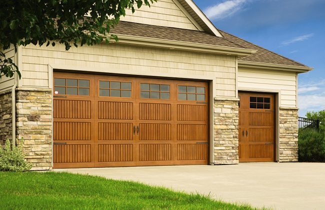 Two-car garage with wooden doors and stone accents, set in a modern suburban home on a sunny day.
