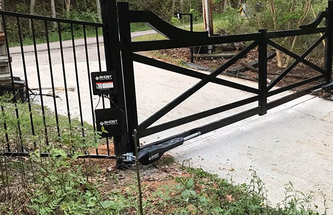 Automatic driveway gate with black metal frame surrounded by lush greenery.
