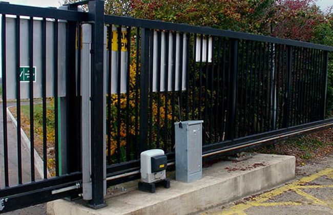 Black automatic sliding gate with motor, outdoor installation, surrounded by greenery for security and access control.