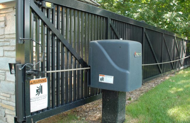 Automatic sliding gate with a security warning sign in a landscaped area.