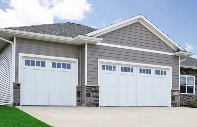 Modern suburban house with two-car garage, white doors, and stone accents under a blue sky.