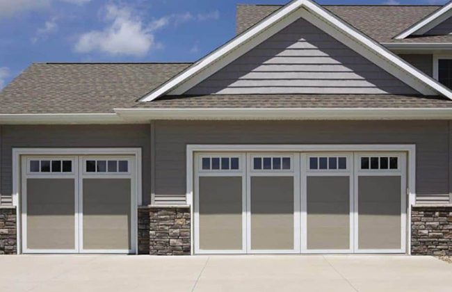 Modern house with three-car garage, stone accents, and gray siding under a clear blue sky.