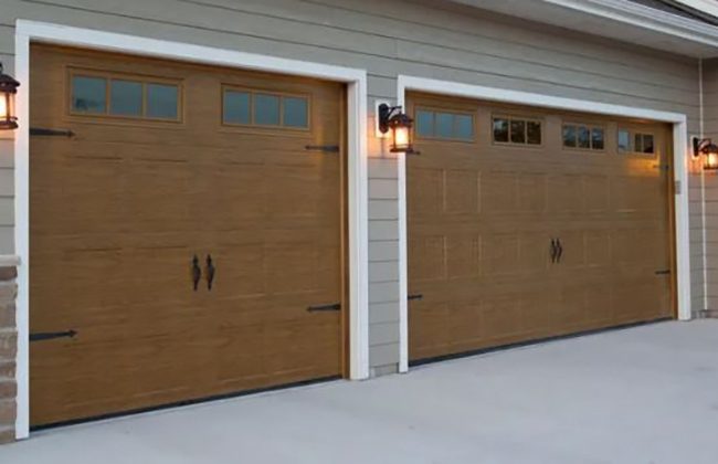 Two wooden garage doors with decorative windows and exterior lights on a modern house.
