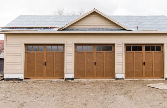 Three-car garage with wooden doors under construction on a dirt lot.