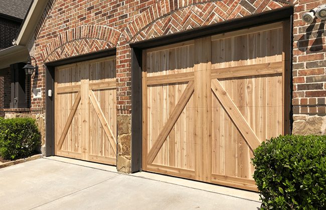 Wooden garage doors on a brick house exterior with driveway and greenery.