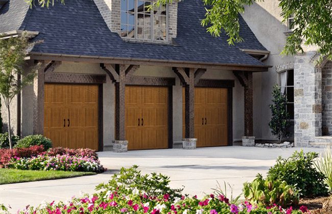 Elegant home exterior with triple wooden garage doors and vibrant garden landscaping.