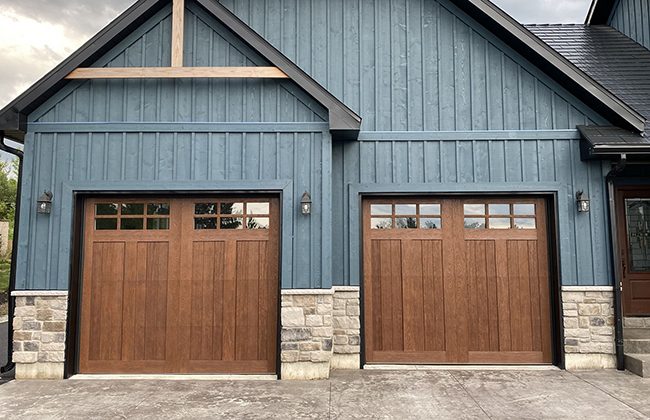 Blue house with two wooden garage doors and stone accents, featuring modern design and lighting fixtures.