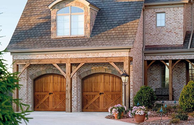 Elegant brick house with wooden garage doors, decorative lantern, and blooming garden in front.